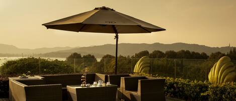 A deck with wicker furniture, a table with a teapot, and a large umbrella.