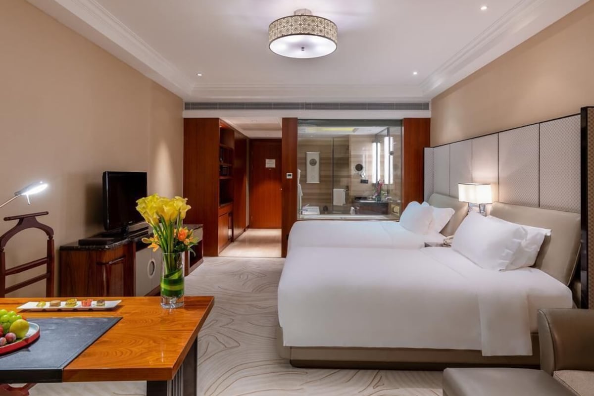 Een hotelkamer met twee bedden, een bureau met lamp, een televisie en uitzicht op de badkamer.