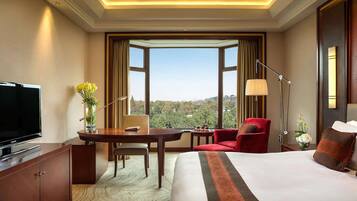 A hotel room with a large bed, a desk with a chair, a television, and a view of the city.
