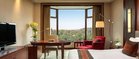 A hotel room with a large bed, a desk with a chair, a television, and a view of the city.