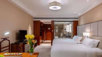 Een hotelkamer met een bed, een bureau met lamp, een televisie en een vaas met bloemen.