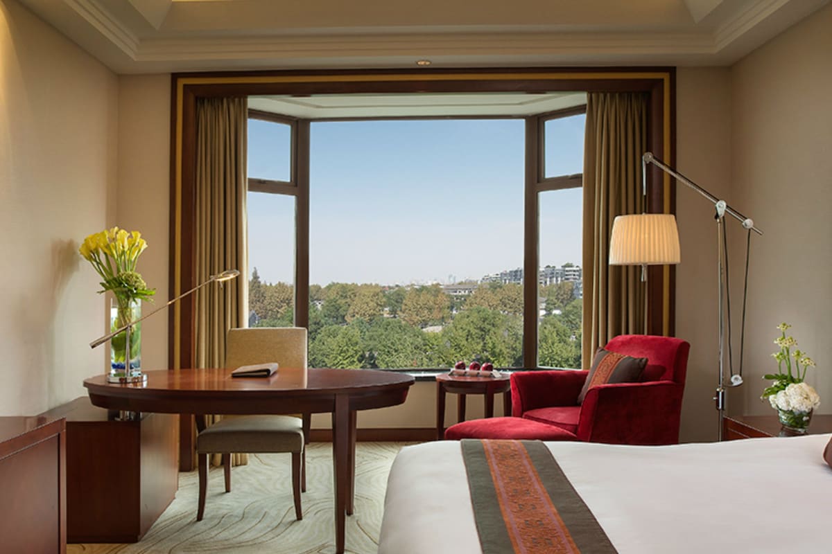 Een hotelkamer met een groot bed, een bureau, een stoel, een lamp en uitzicht op de stad.