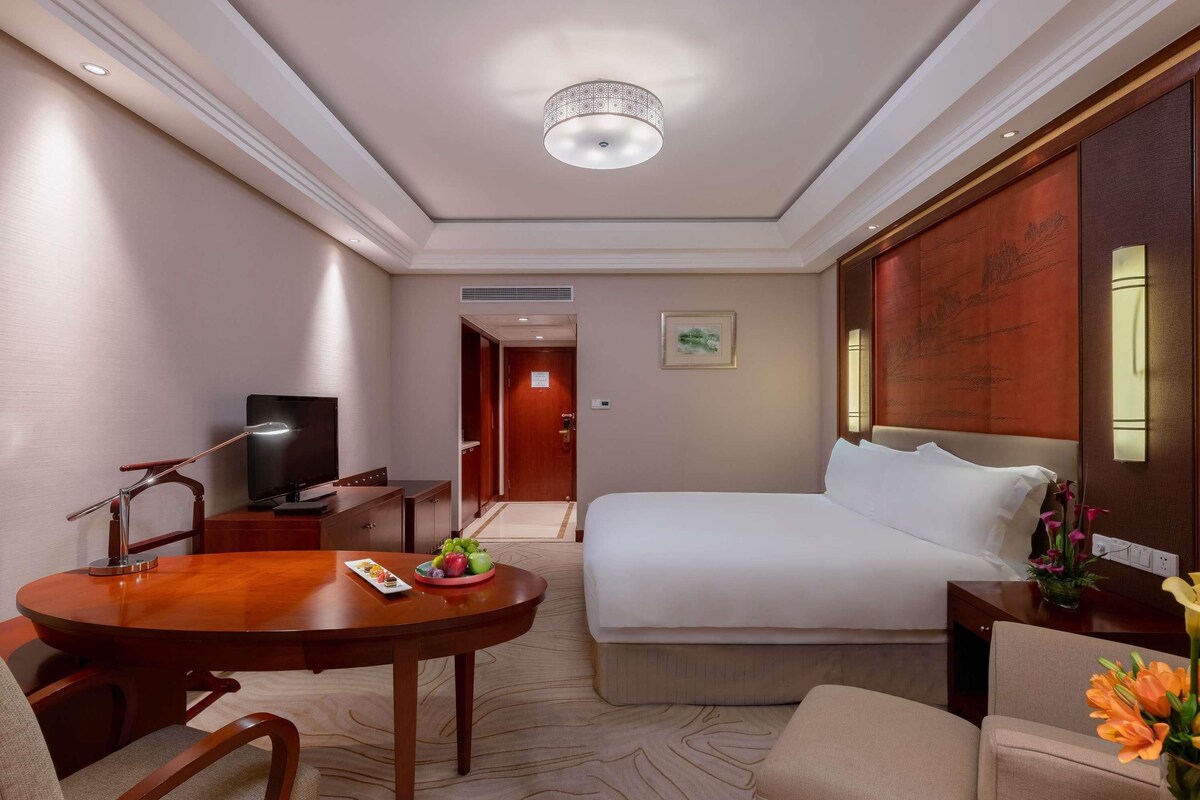 Une chambre d’hôtel comprenant un lit, un bureau avec une télévision, une table à manger avec des chaises et un sol recouvert de moquette.
