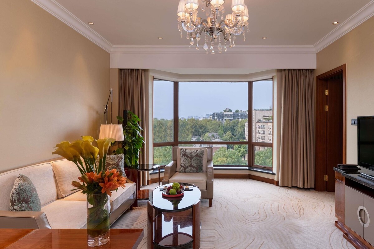 Une chambre d’hôtel moderne dotée d’une grande fenêtre, d’un lustre, d’un canapé, d’une table à manger et d’un téléviseur.