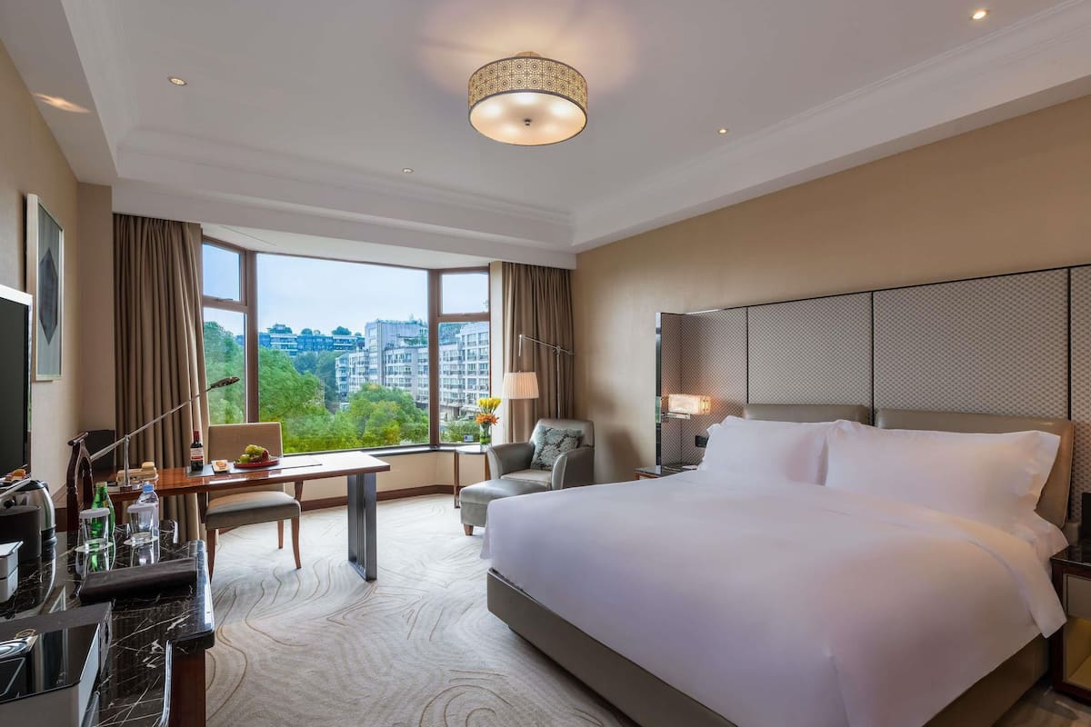 Ein Hotelzimmer mit einem großen Bett, einem Schreibtisch mit Stuhl, einem Fernseher und Blick auf die Stadt.