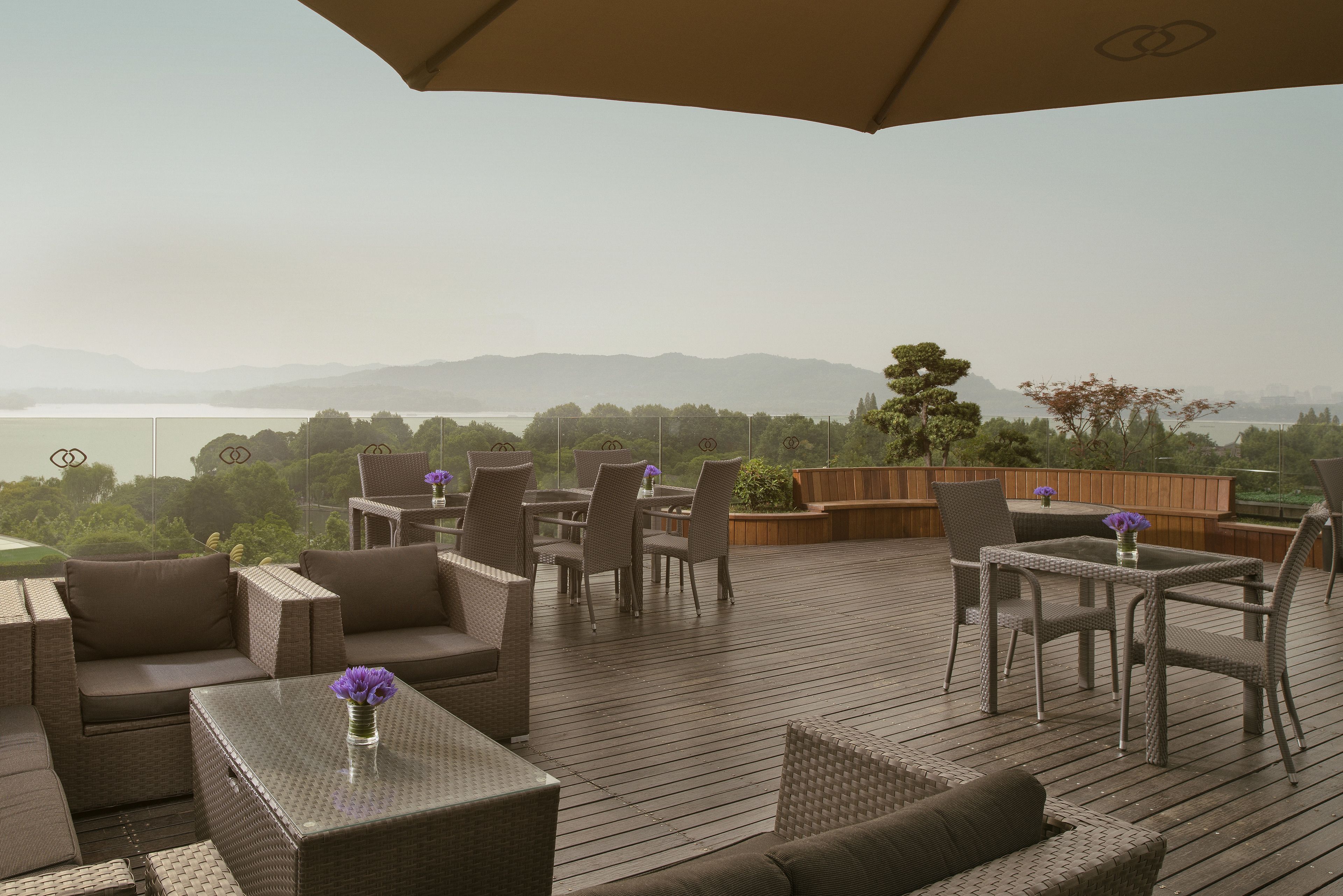 A deck with wicker furniture, a table with a vase of flowers, and a view of a lake and mountains.