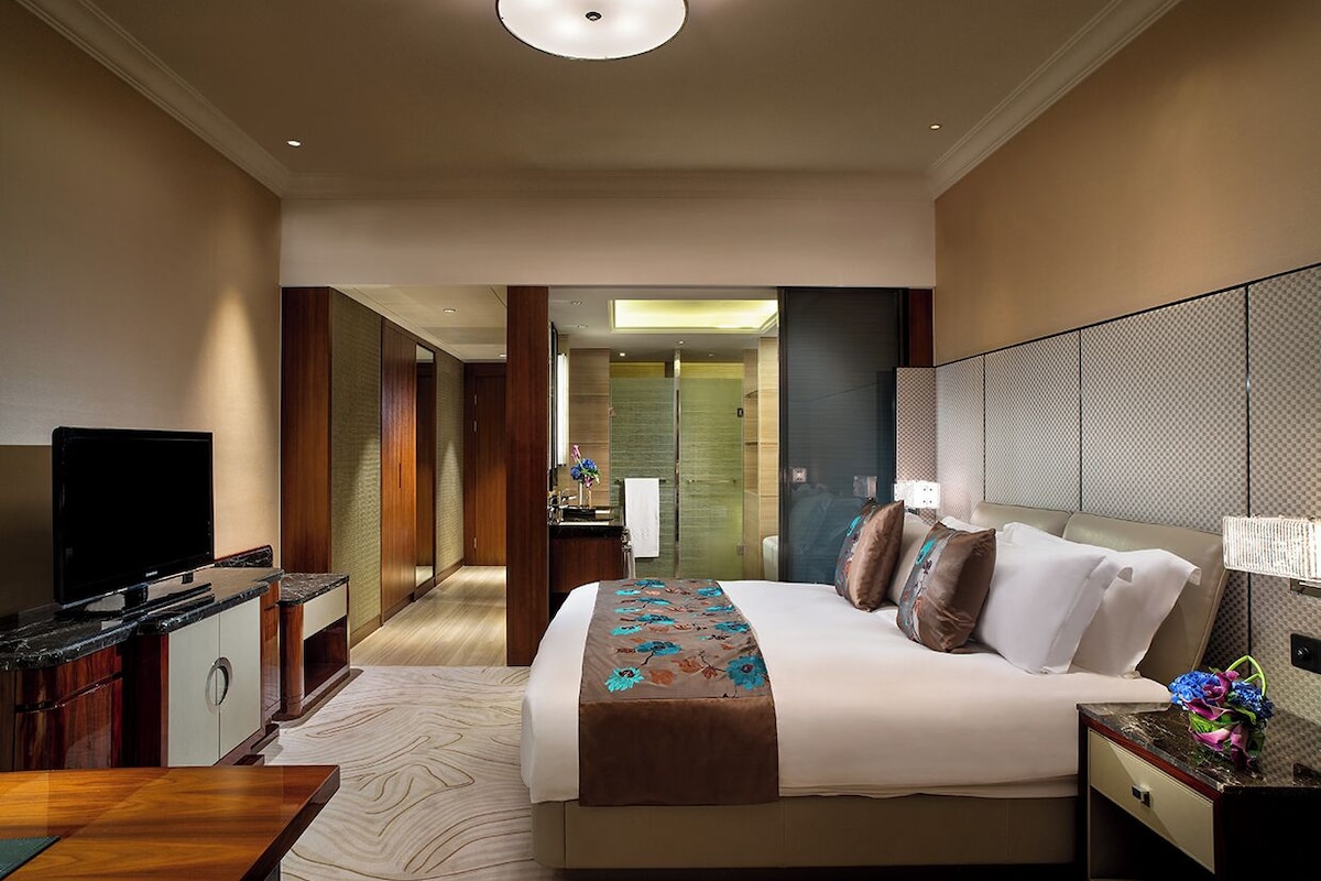 Een hotelkamer met een bed, een televisie, een bureau en een badkamer zichtbaar door een geopende deur.