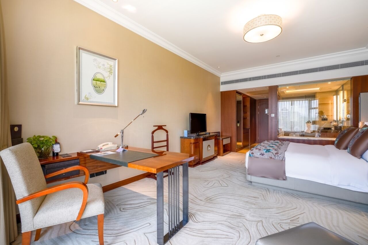 A hotel room with a bed, a desk with a chair, a television, and a framed picture on the wall.