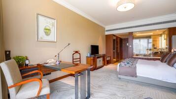 A hotel room with a bed, a desk with a chair, a television, and a framed picture on the wall.