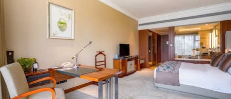A hotel room with a bed, a desk with a chair, a television, and a framed picture on the wall.