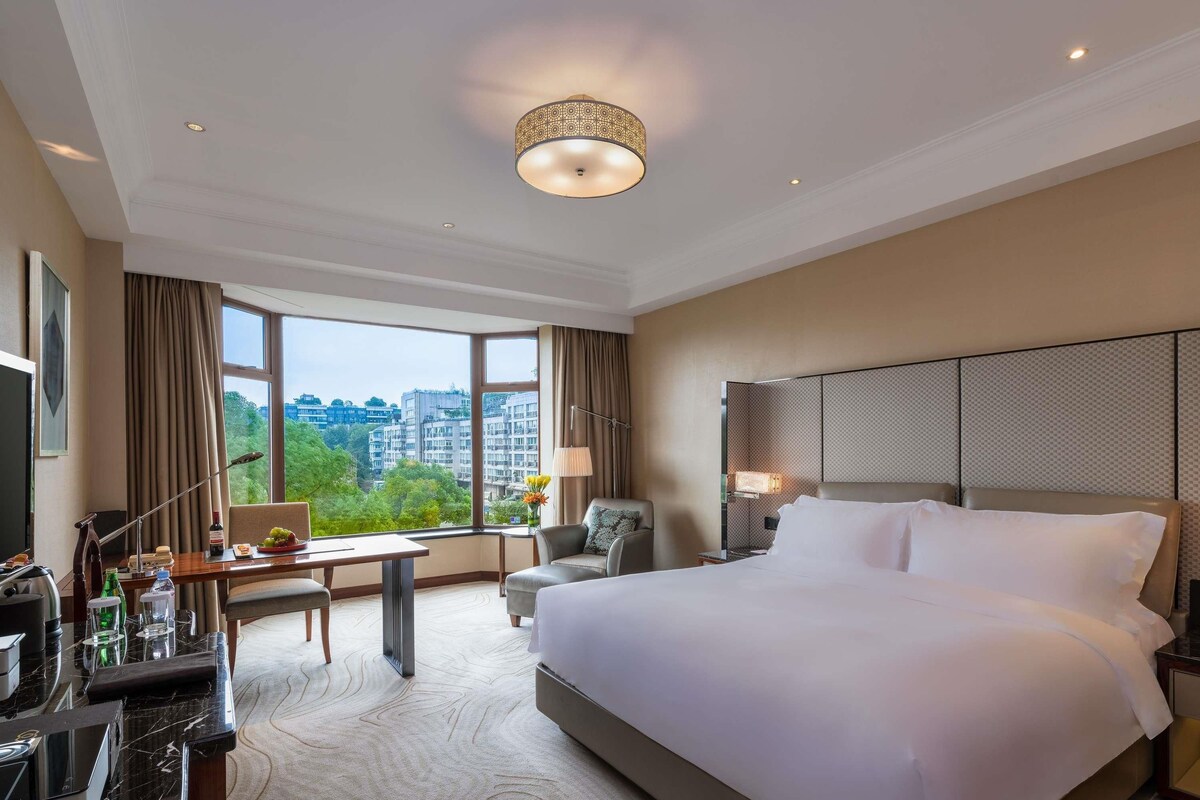 Une chambre d’hôtel avec un grand lit, un bureau avec une chaise, une télévision et une vue sur le paysage urbain.