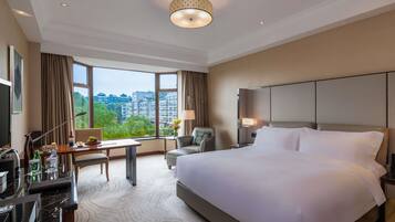 A hotel room with a large bed, a desk with a chair, a TV, and a view of the cityscape.