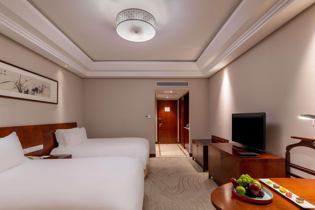 Une chambre d’hôtel avec deux lits, une télévision, un bureau et une table à manger avec des fruits.