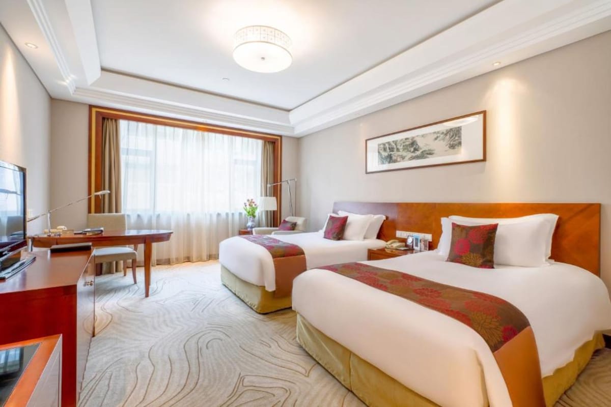 Een hotelkamer met twee bedden, een bureau, een televisie en een groot raam met gordijnen.