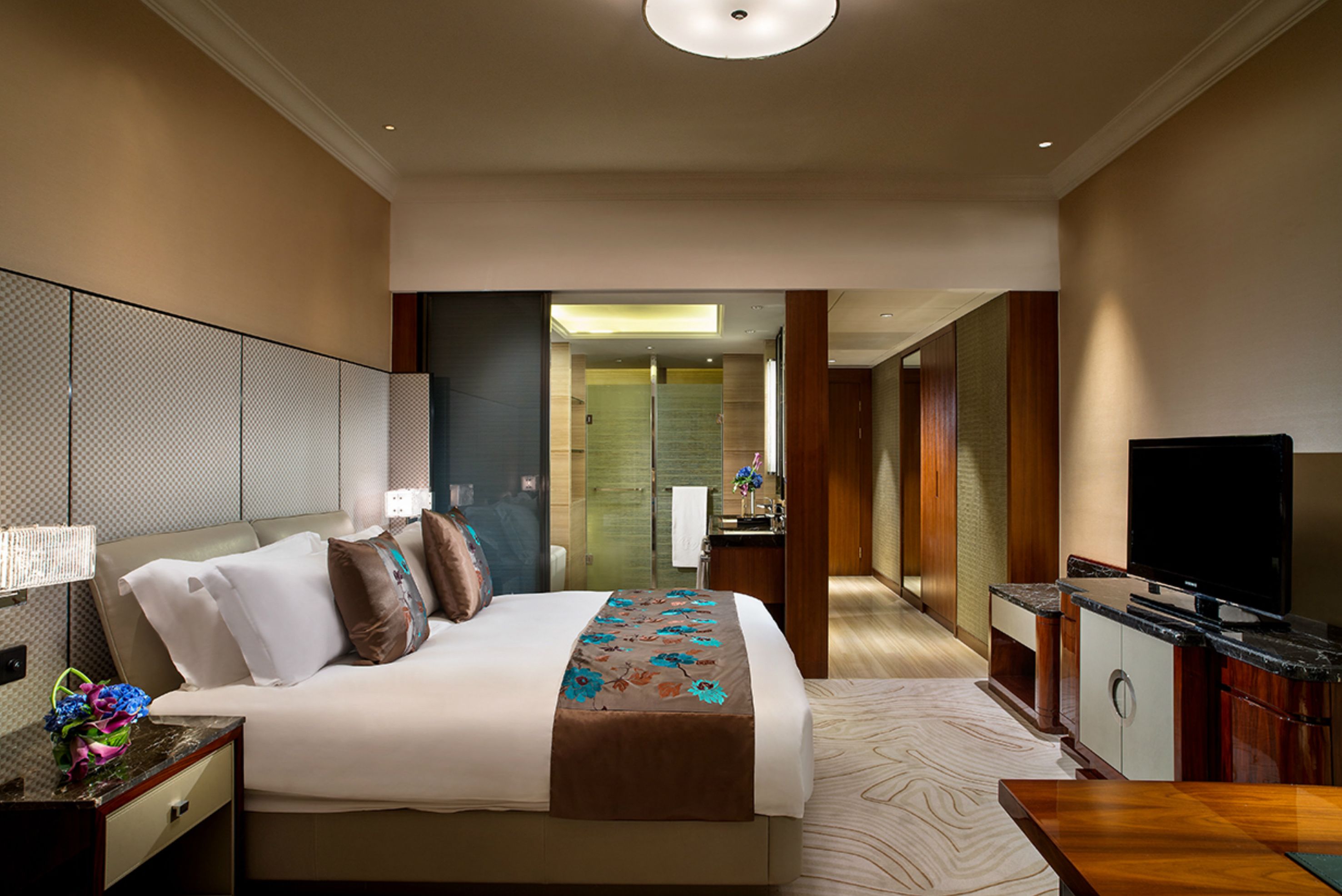 A hotel room with a large bed, a TV, a desk, and a bathroom visible through an open door.