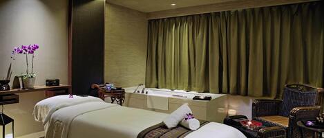 Ein Hotelzimmer mit Bett, kleinem Tisch, Stuhl, Spiegel, Fenster mit Vorhängen und Nachttisch mit Lampe und Pflanze.
