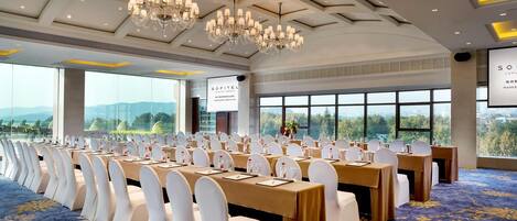 Un salón de conferencias con mesas y sillas, amplias ventanas, candelabros y suelo alfombrado.