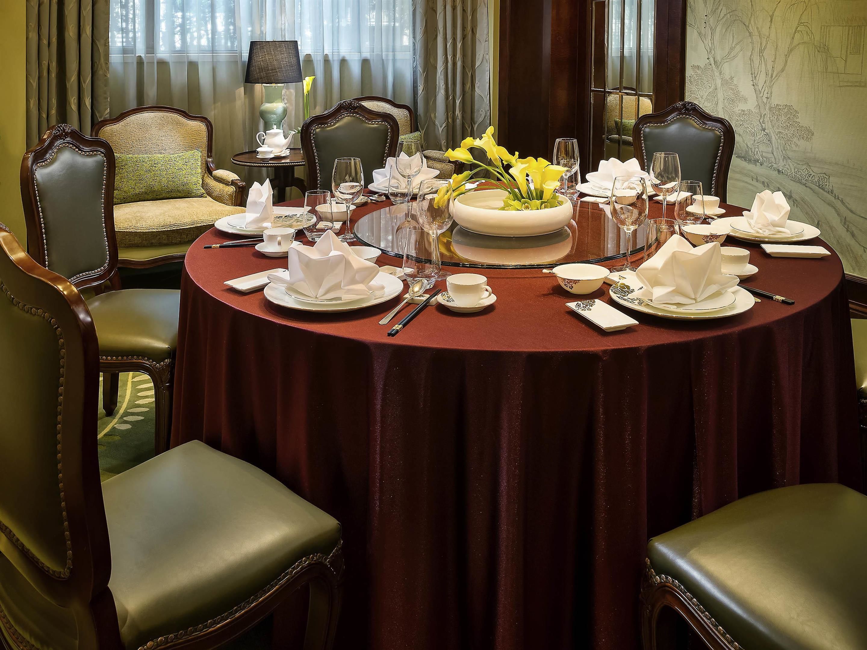 Une salle à manger élégante, avec une table ronde dressée pour le repas, entourée de chaises rembourrées.