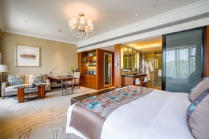 Une chambre d’hôtel avec un grand lit, un bureau, un canapé, un lustre et une salle de bain équipée d’un miroir et d’un lavabo.