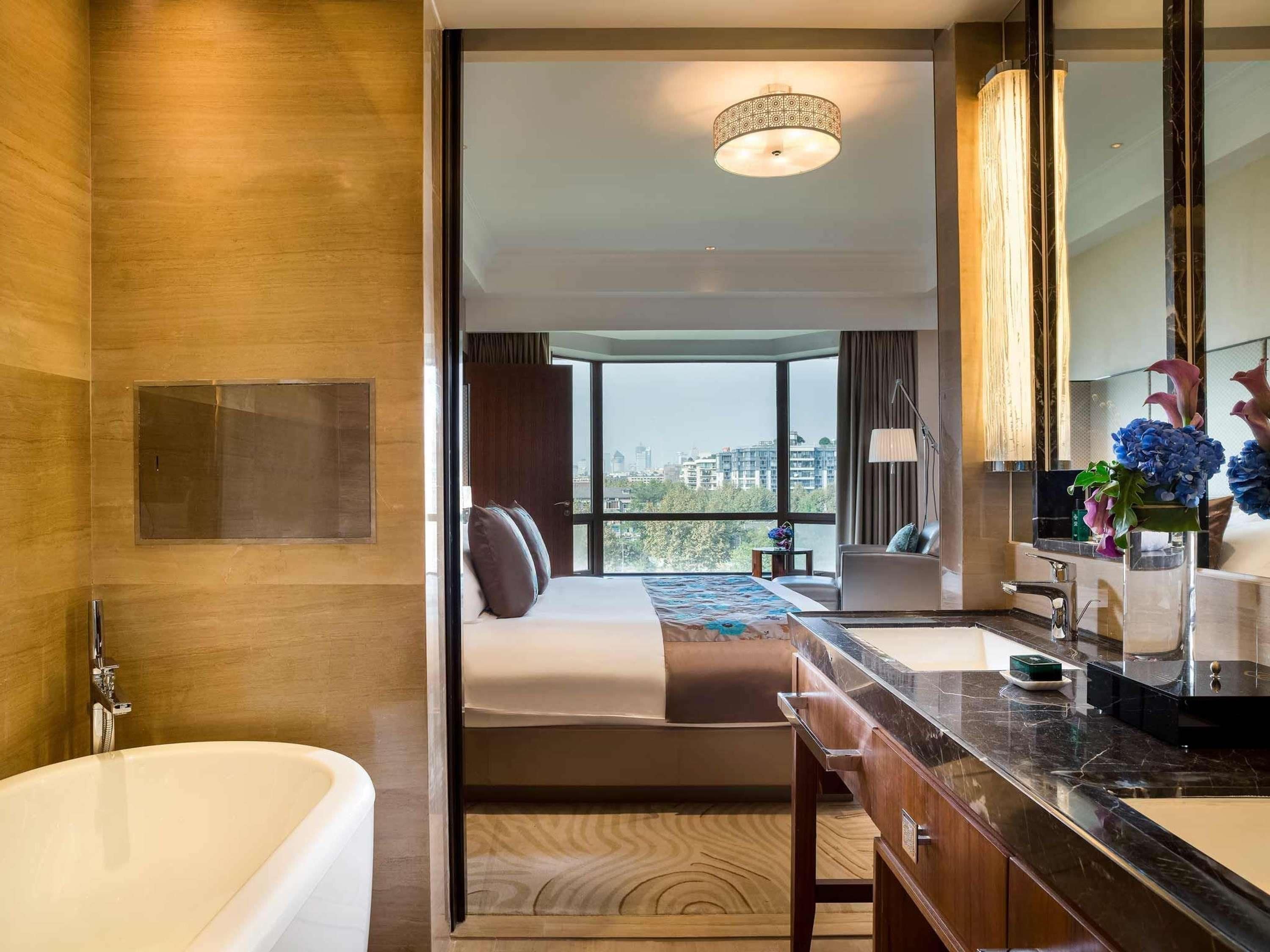 Une chambre d’hôtel moderne dotée d’un grand lit, d’une salle de bain avec baignoire, d’une coiffeuse avec miroir et offrant une vue sur la ville.