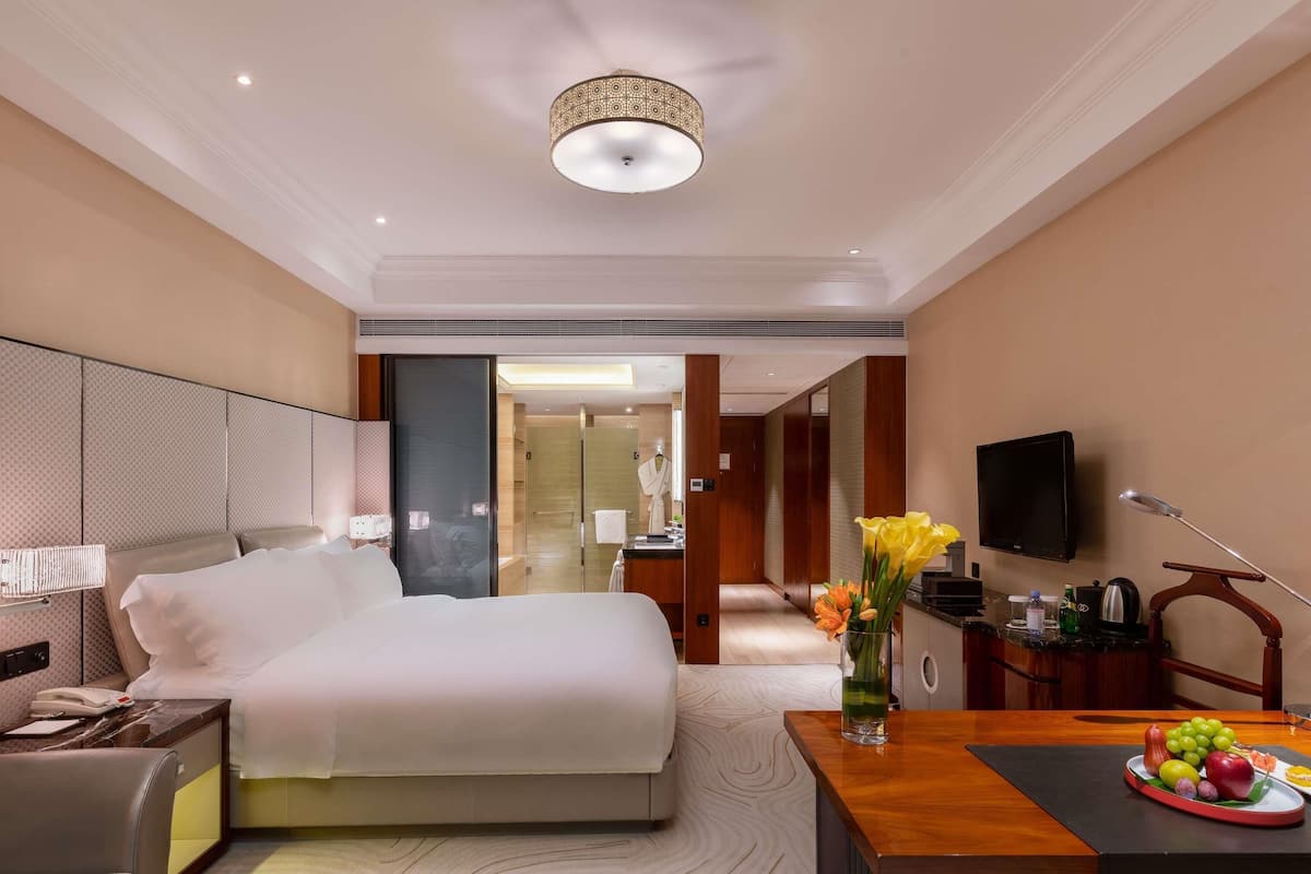 Ein Hotelzimmer mit Bett, Nachttisch, Lampe, Fernseher und einer Essecke für zwei Personen.