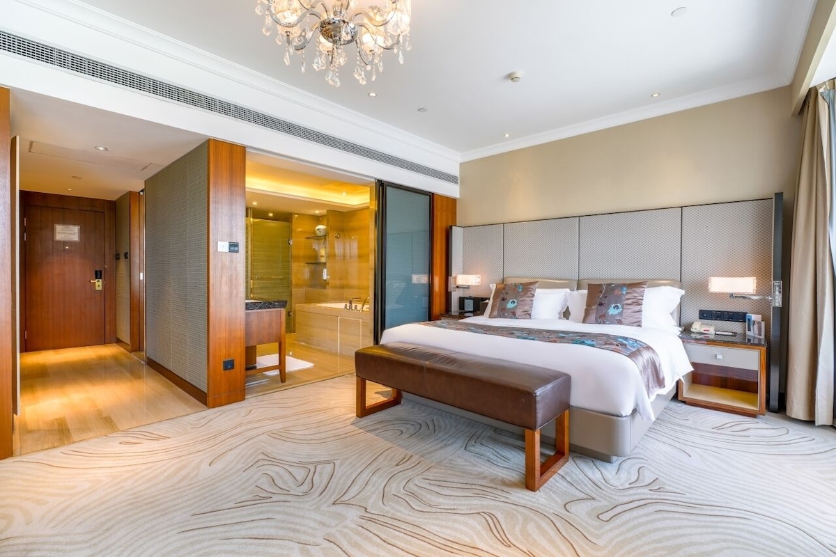 Een moderne hotelkamer met een groot bed, een bankje, een inloopkast en een badkamer met een bad.