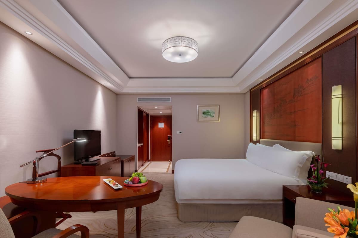 Ein Hotelzimmer mit einem Bett, einem Schreibtisch mit Fernseher, einem Esstisch mit Stühlen und einem Teppichboden.