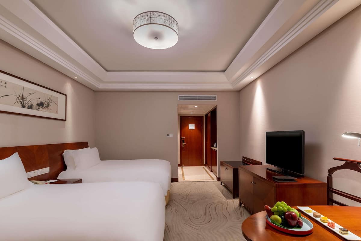 Ein Hotelzimmer mit zwei Betten, einem Fernseher, einem Schreibtisch und einem Esstisch mit Obst.