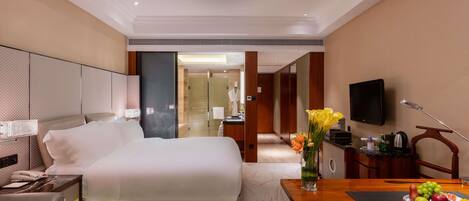 A hotel room with a bed, bedside table, lamp, TV, and a dining area with a table set for two.