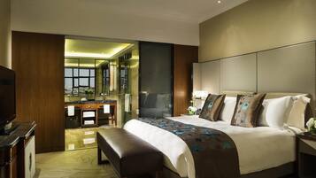 Una habitación de hotel moderna con una cama grande, un banco, un televisor, un baño con espejo y vistas a la ciudad.