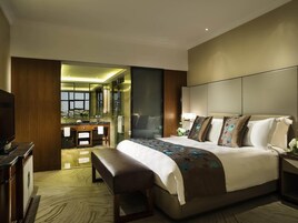 Una habitación de hotel moderna con una cama grande, un banco, un televisor, un baño con espejo y vistas a la ciudad.