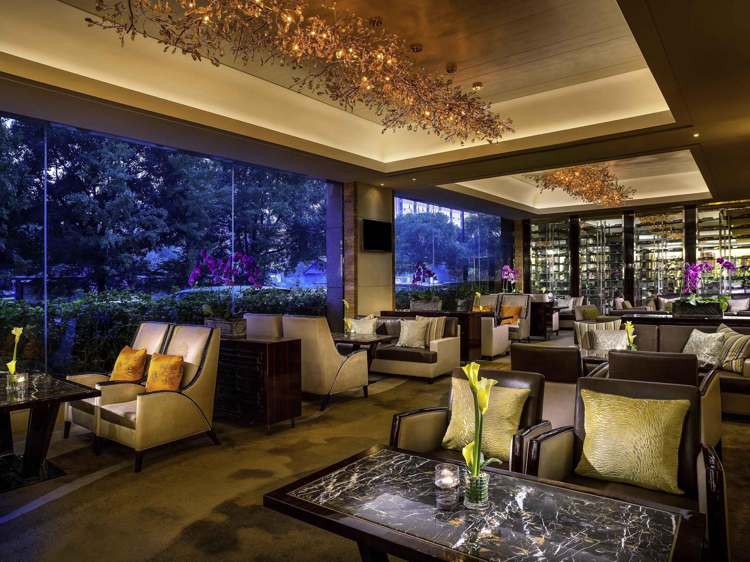 A modern lounge area with comfortable seating, a marble coffee table, and large windows offering a view of a garden at night.