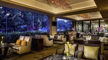 A modern lounge area with comfortable seating, a marble coffee table, and large windows offering a view of a garden at night.