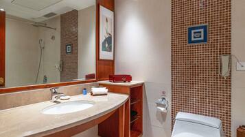 A bathroom with a large mirror, two sinks, a shower, and a toilet.