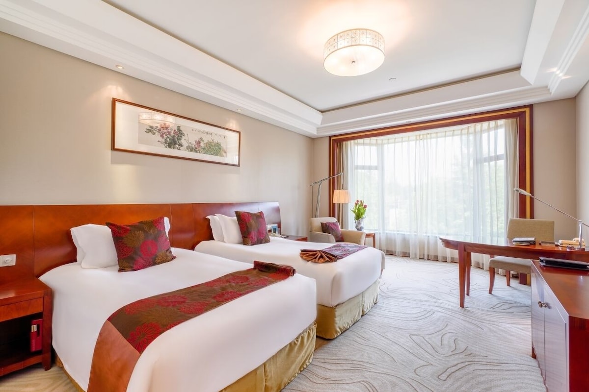 Een hotelkamer met twee bedden, een bureau, een stoel en een groot raam met gordijnen.