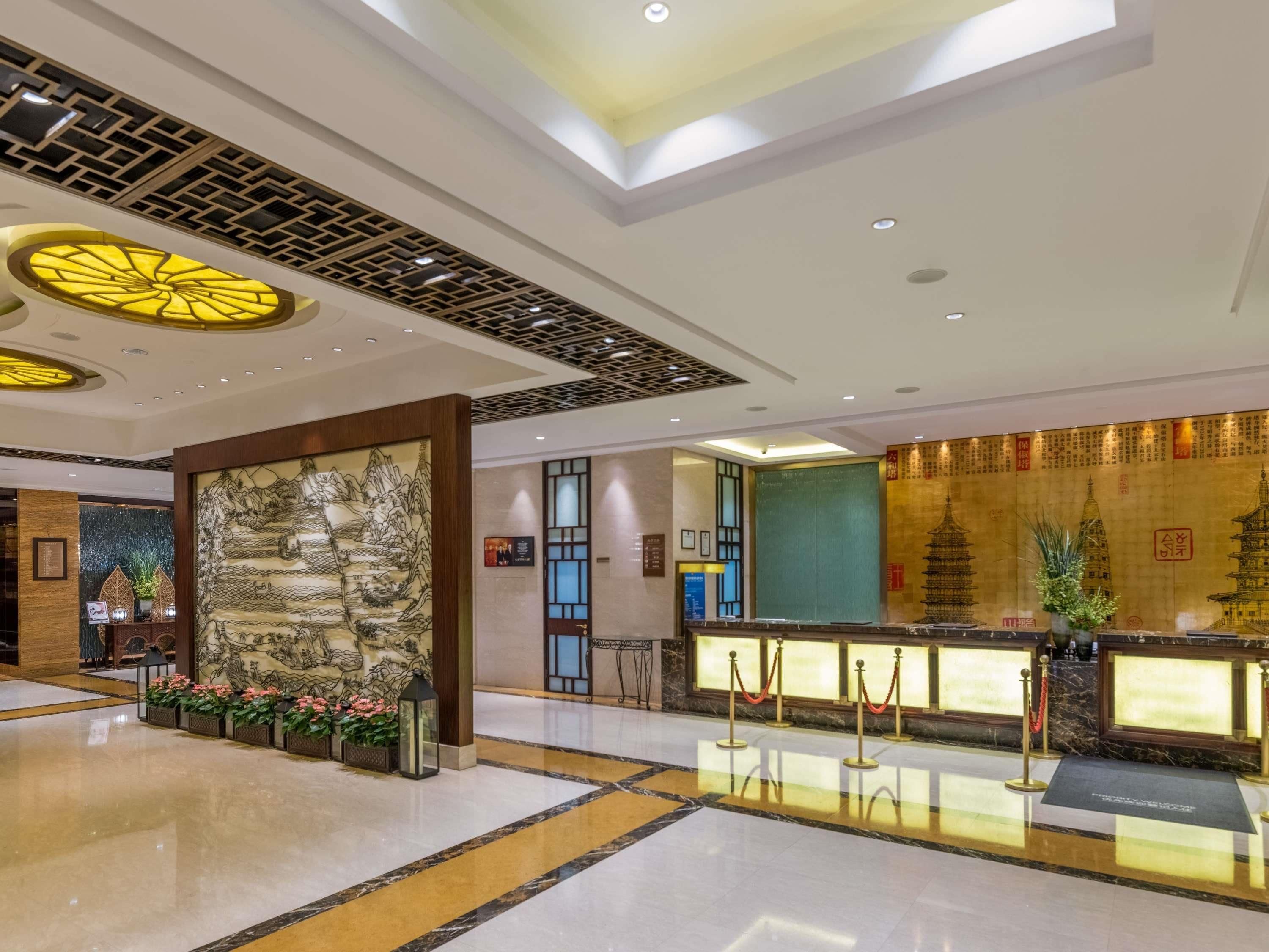 A hotel lobby with a reception desk, a large mural, and a traditional Chinese architectural ceiling design.