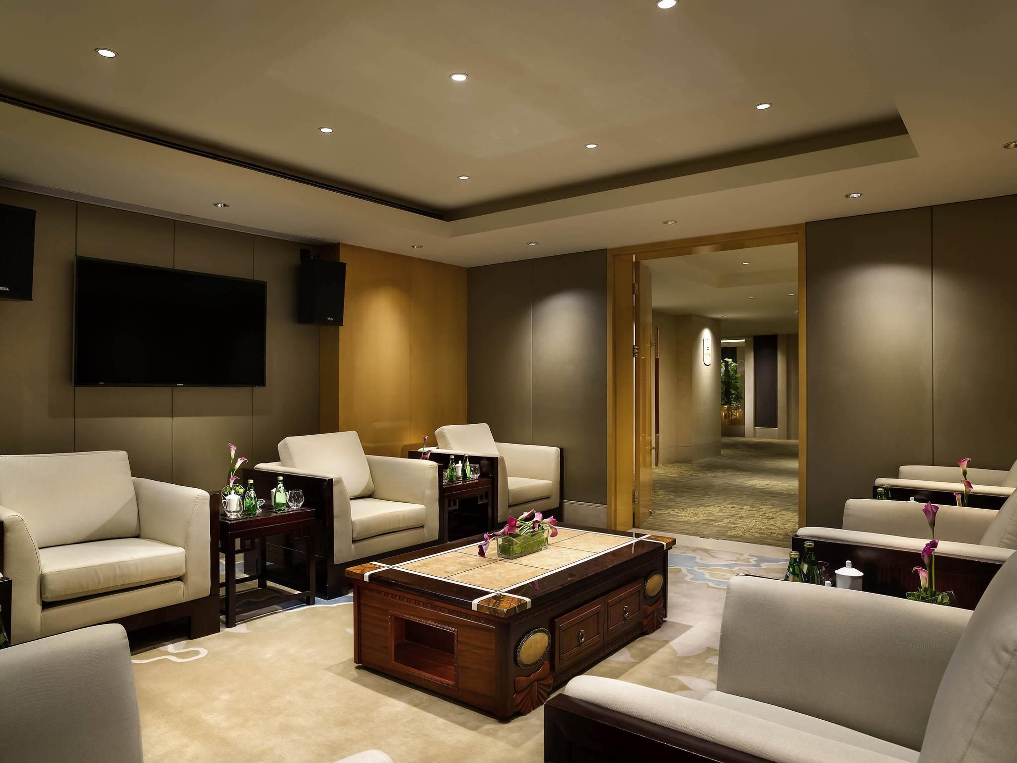 A modern living room with a large flat-screen TV, comfortable seating, a coffee table, and a hallway leading to another room.
