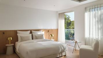 A modern hotel room with a large bed, two bedside tables with lamps, a chair, and a balcony with curtains.