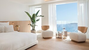 A modern hotel room with a large bed, two armchairs, a small table, and a potted plant.