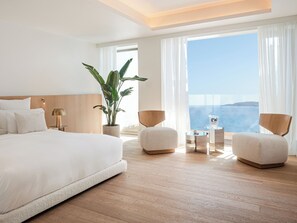 A modern hotel room with a large bed, two armchairs, a small table, and a potted plant.