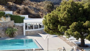 A poolside area with a clear view of a swimming pool, lounge chairs, and a modern building with a stone facade.