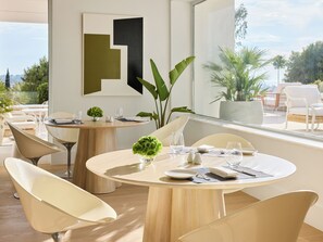A modern dining area with round tables, white chairs, and a view of the outdoors.