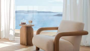 Habitación con vista al mar, piso de madera, un sillón color beige y una mesita con adornos.