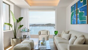 A modern living room with a large window, a sofa, ottomans, a coffee table, and a potted plant.