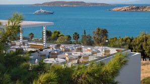 A rooftop terrace with outdoor seating, overlooking a coastal area with a yacht and distant islands.