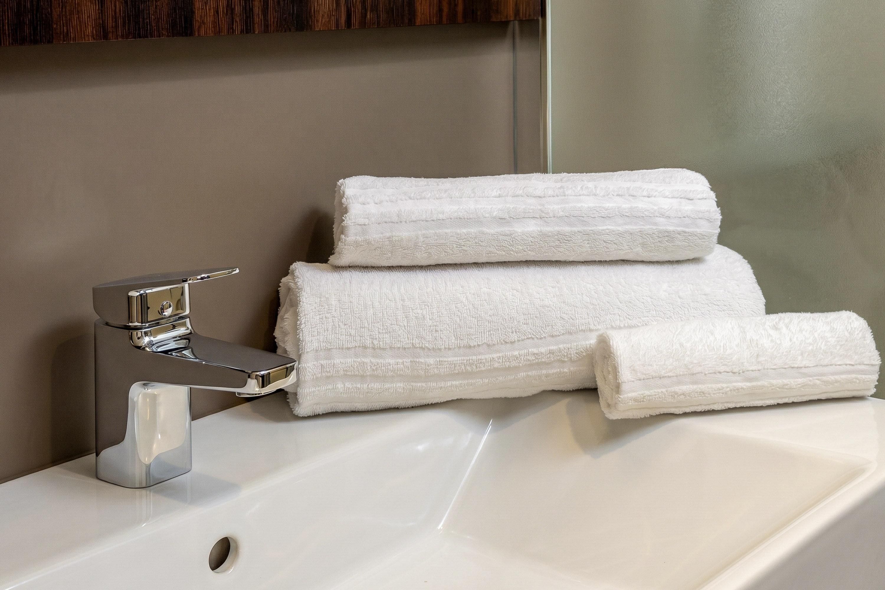 A bathroom with a chrome faucet and a stack of white towels.