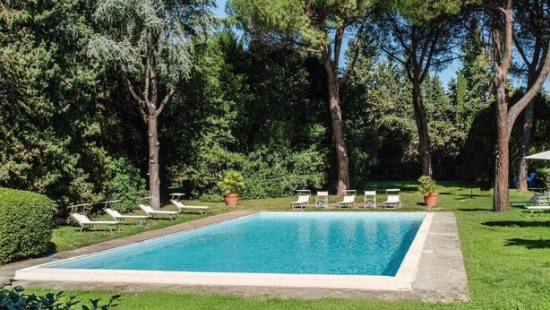 A rectangular swimming pool with a stone border, surrounded by a well-maintained lawn and trees. - B&B HOTEL CALENZANO FIRST (Calenzano)