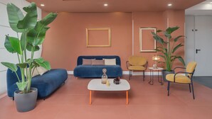 A modern living room with a blue sofa, a coffee table, and two chairs. There are large potted plants and framed pictures on the walls. - B&B HOTEL CALENZANO FIRST (Calenzano)
