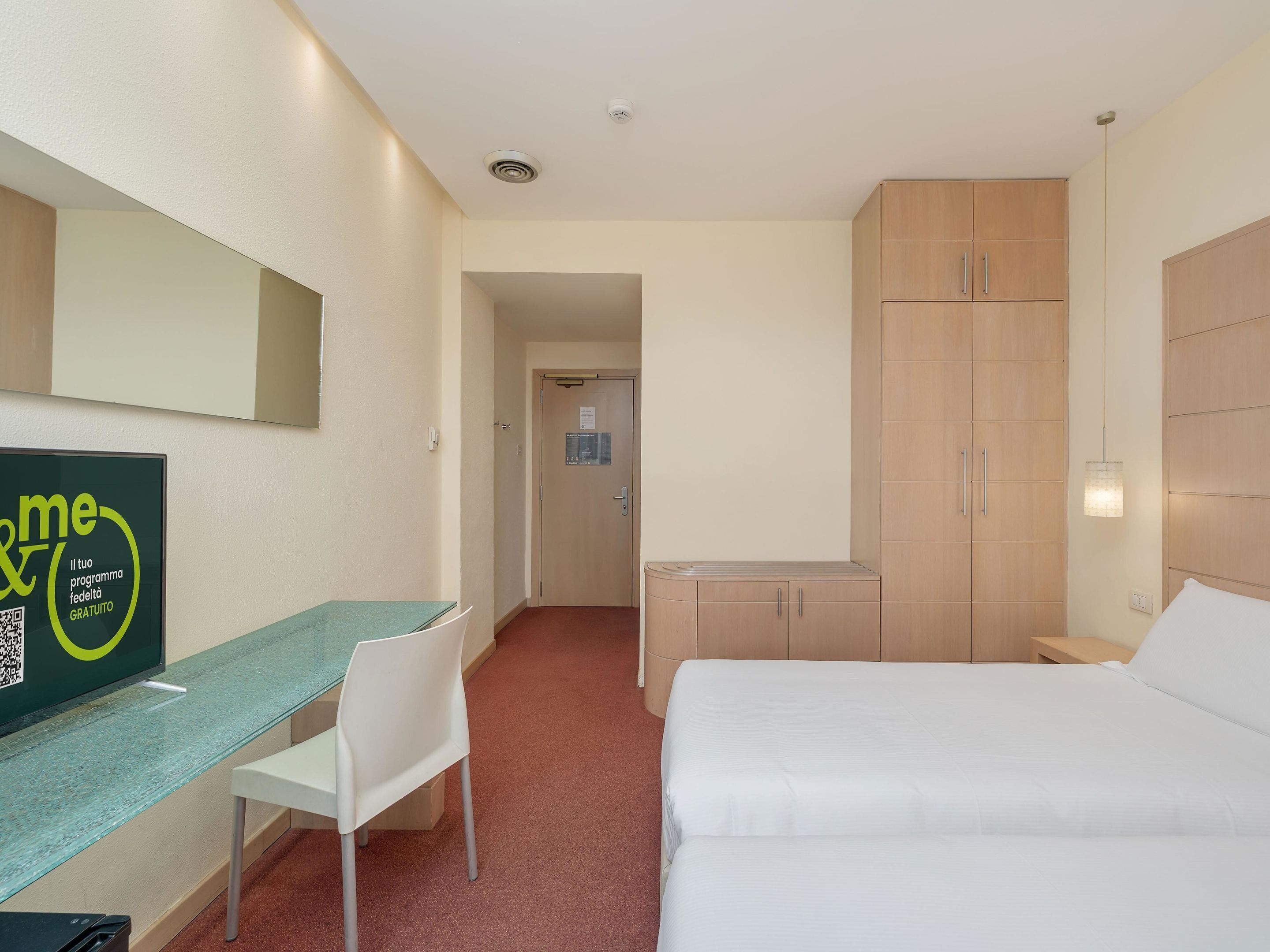 A hotel room with a bed, a desk, a chair, and a wardrobe.