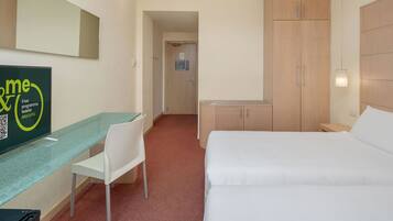 A hotel room with a bed, a desk, a chair, and a wardrobe.